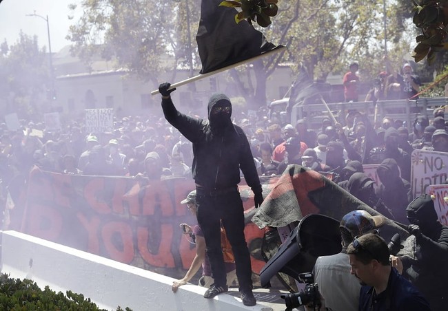 An anti-fascist demonstrator jumps over a barricade during a free speech rally Sunday, Aug. 27, 2017, in Berkeley, Calif. Several thousand people converged in Berkeley Sunday for a "Rally Against Hate" in response to a planned right-wing protest that raised concerns of violence and triggered a massive police presence. Several people were arrested for violating rules against covering their faces or carrying items banned by authorities. (AP Photo/Marcio Jose Sanchez)