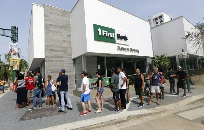FILE - In this Wednesday, Sept. 27, 2017, file photo, people wait in line to withdraw cash at a bank in the aftermath of Hurricane Maria, in San Juan, Puerto Rico. Maria has thrown Puerto Rico’s already messy economic recovery plans into disarray. (AP Photo/Gerald Herbert, File)